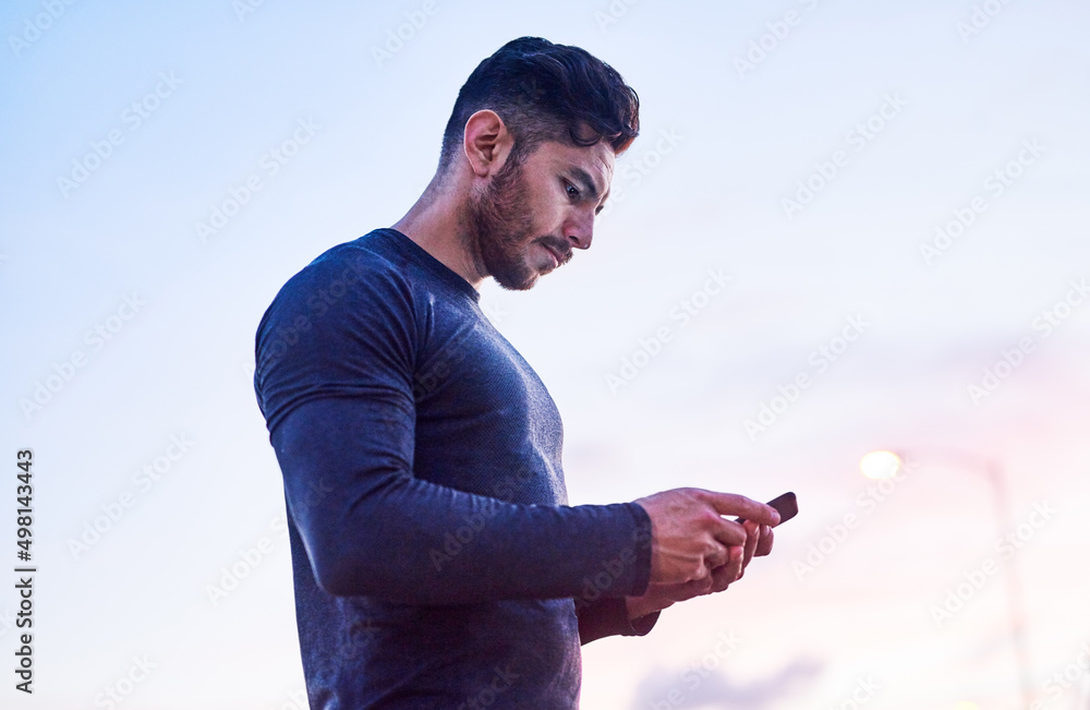 Just finished with another great run. Shot of a sporty young man using a cellphone outdoors.