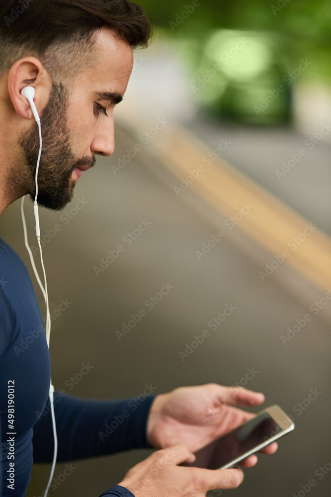 准备好他的锻炼播放列表。一个英俊的年轻男跑步者检查他的运动包的裁剪镜头