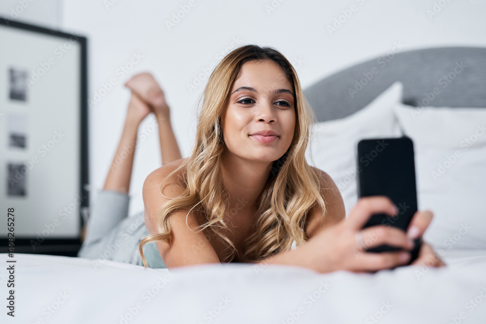 A selfie a day keeps the boredom at bay. Shot of a young woman using her cellphone while lying on he