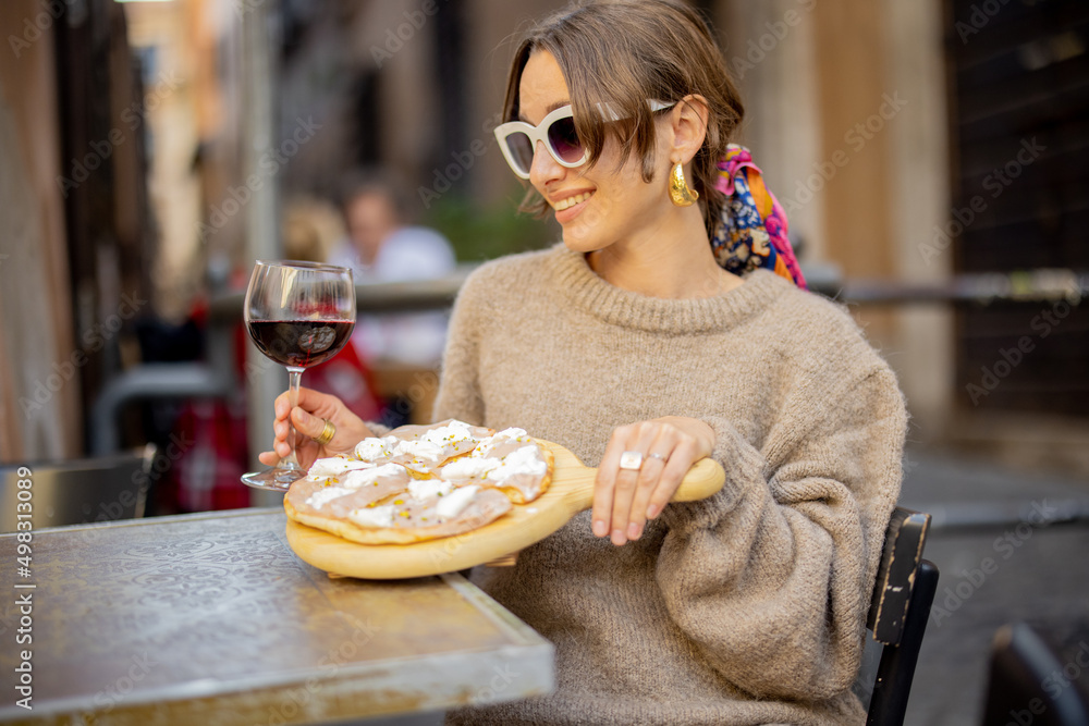 一个女人在罗马一条街上的餐厅吃披萨和喝葡萄酒。意大利美食的概念