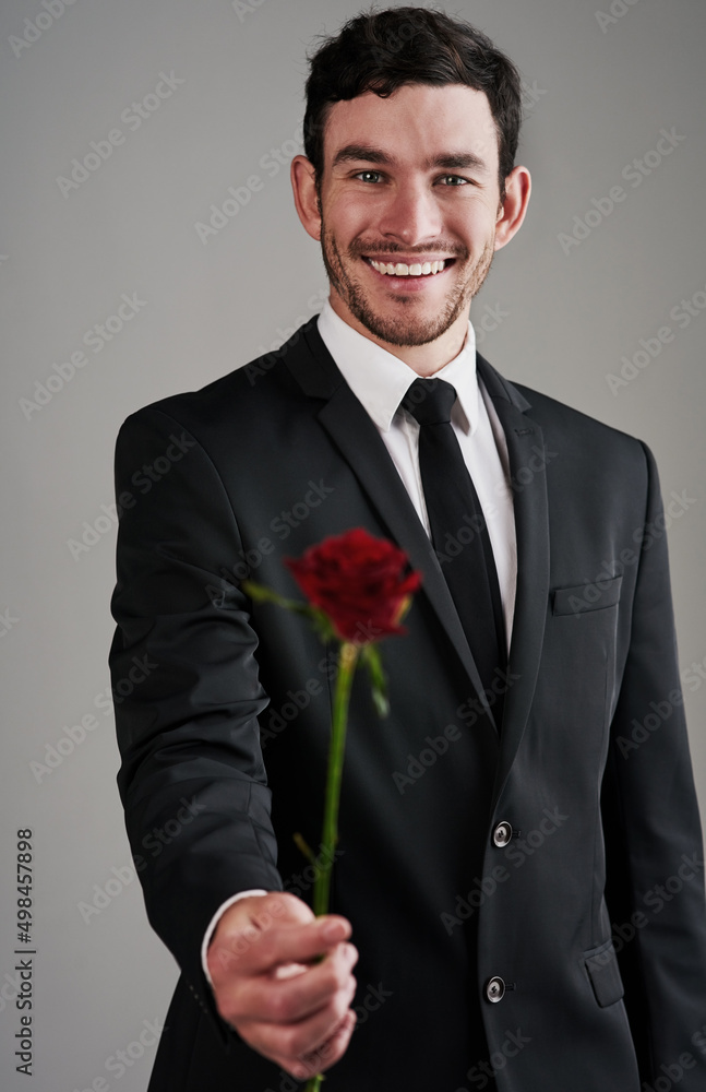 The perfect gentleman. Studio shot of a well-dressed man holding a red rose against a gray backgroun