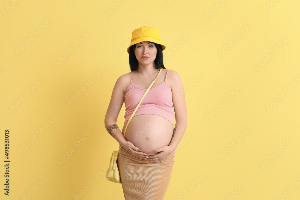 Stylish pregnant young woman on yellow background