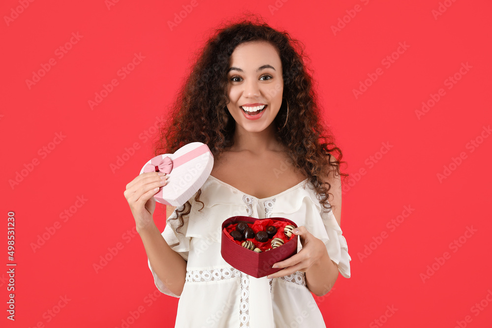 Happy young woman with delicious chocolate candies in box on color background