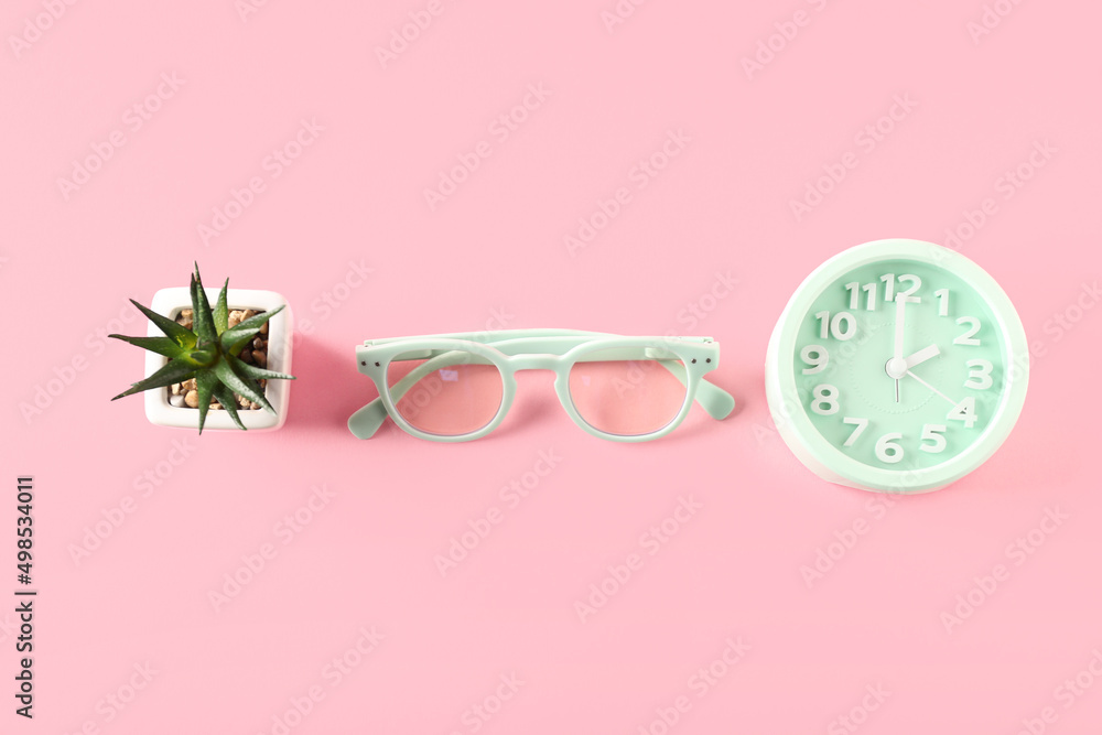 Stylish eyeglasses, alarm clock and houseplant on color background