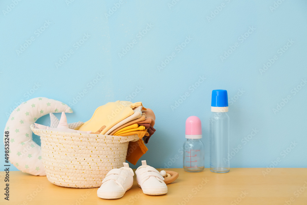 Basket with baby clothes, toys and bottles on table near blue wall