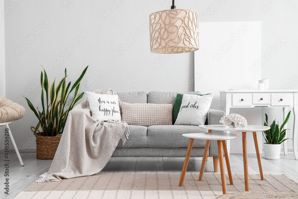 Interior of light living room with coffee tables, sofa and houseplants