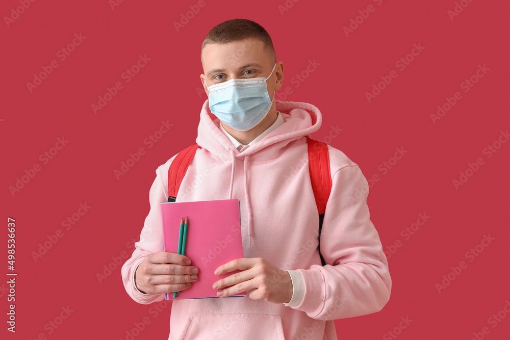 Male student in medical mask with copybooks on red background