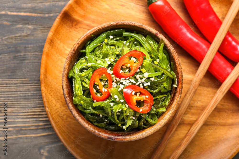 Bowl with healthy seaweed salad and chili pepper on light wooden background