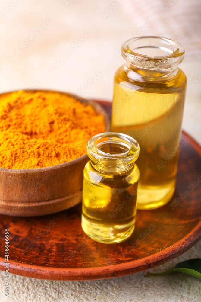 Bottles of oil and turmeric powder on light background