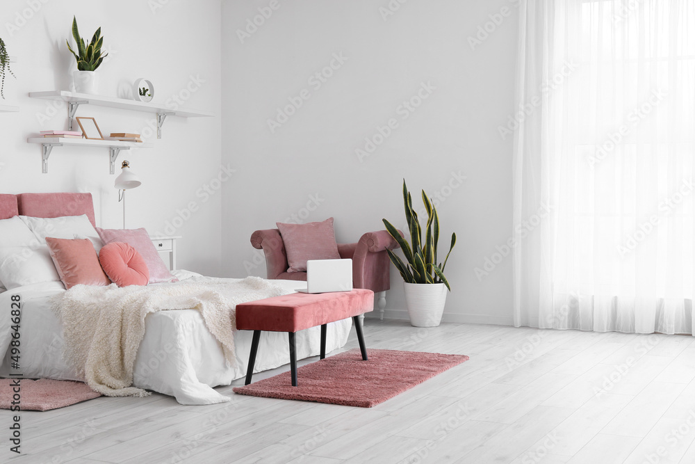 Interior of stylish bedroom with soft ottoman and houseplant