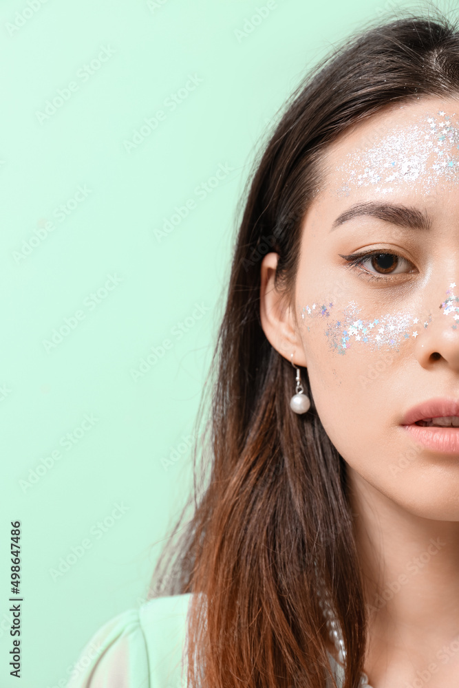 Portrait of Asian woman with glitter makeup and stylish earrings on color background