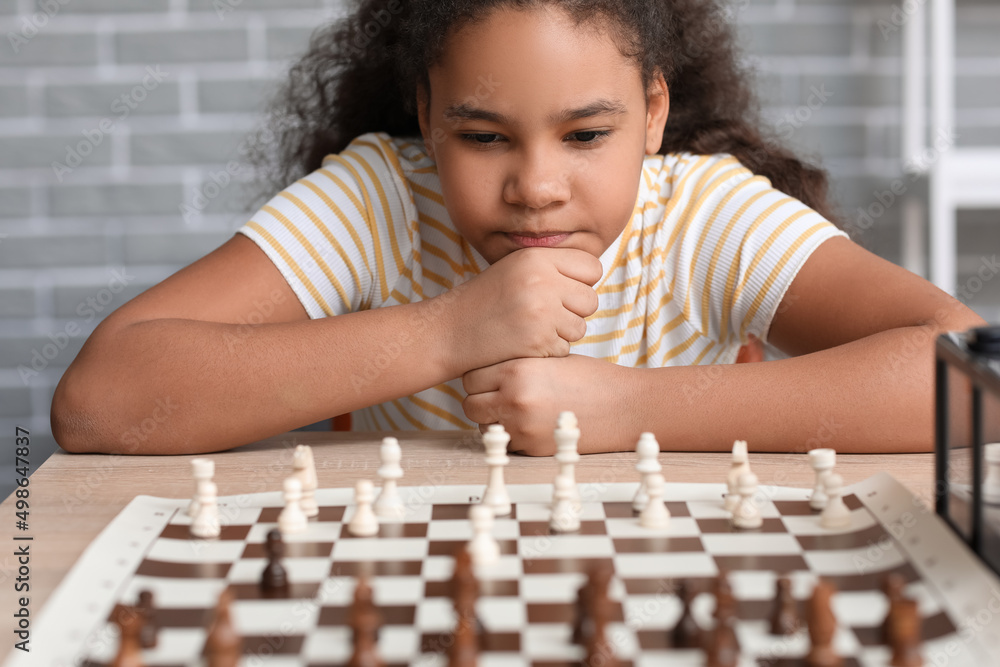 Little African-American girl playing chess during tournament in club