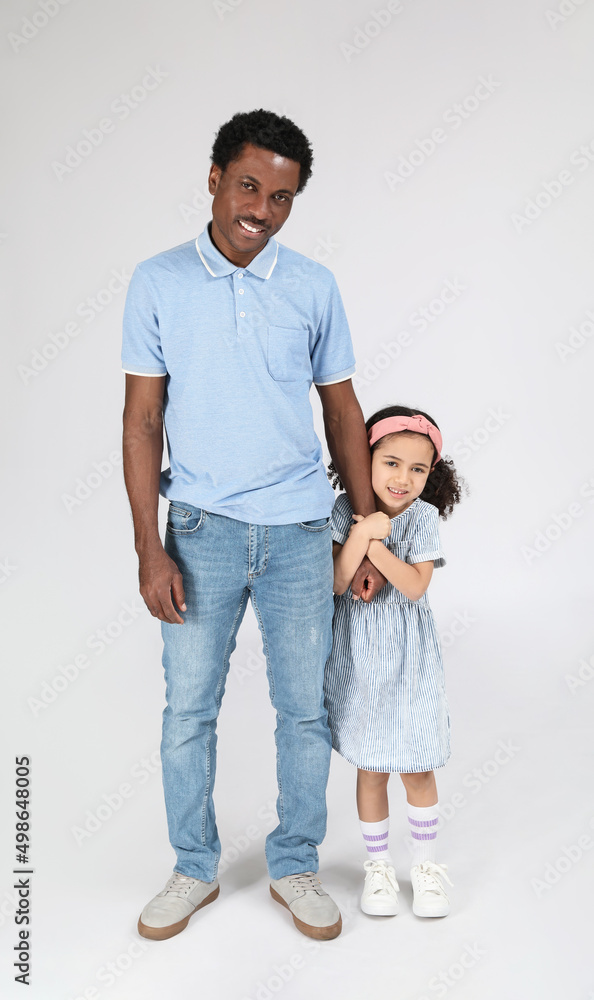 Portrait of little African-American girl and her father on grey background