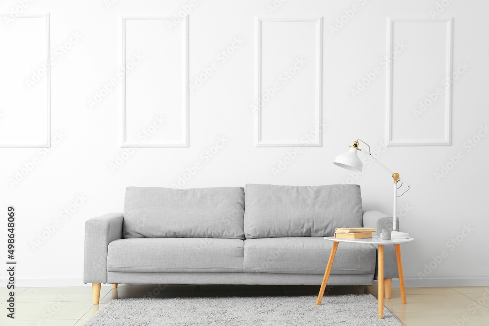 Stylish sofa and lamp on table near white wall