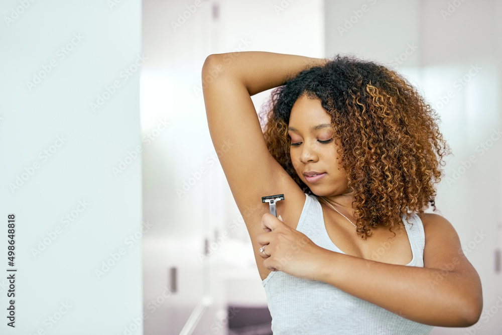 She takes good care of herself. Shot of a confident young woman shaving under her arm pit in the bat