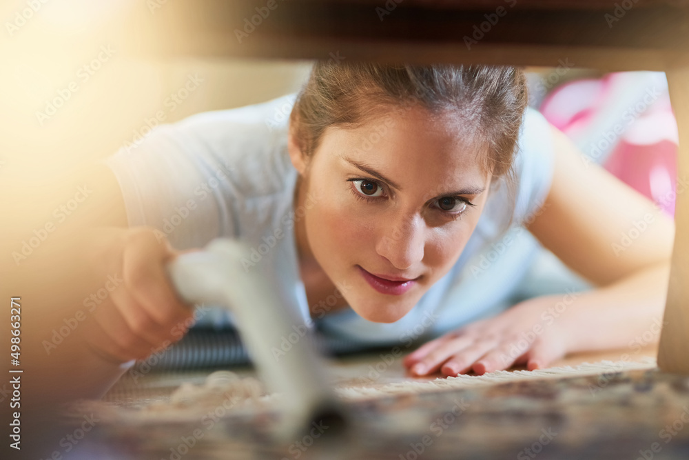 Cleaning those hard to reach places. Closeup shot of a young woman vacuuming underneath a piece of f