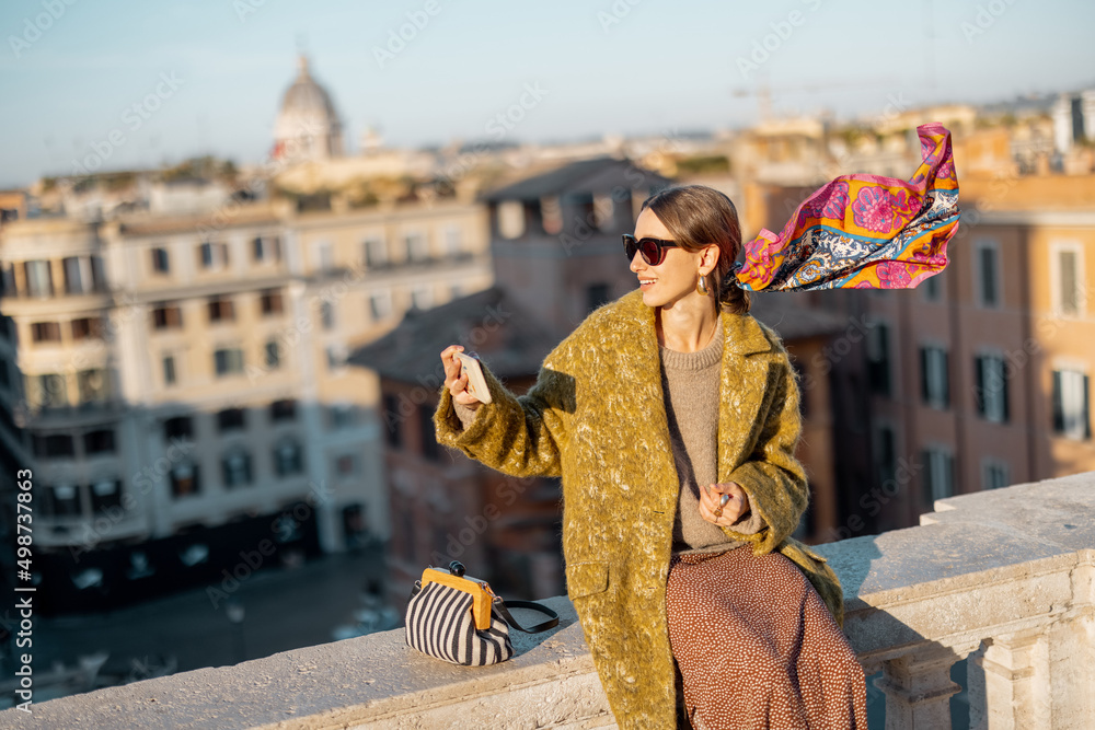 一位女士坐在屋顶上，享受着罗马美丽的早晨城市景观，在手机上拍照