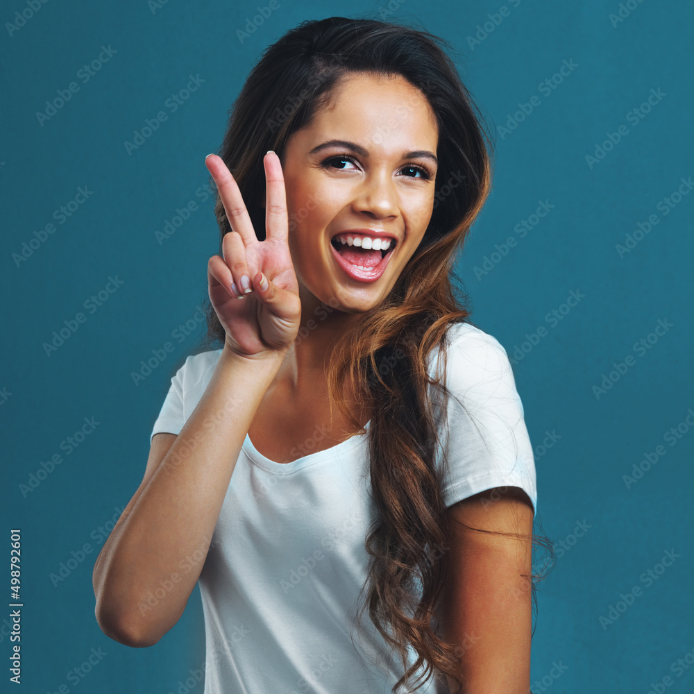 Lifes all good. Studio portrait of an attractive young woman showing a piece sign against a blue bac