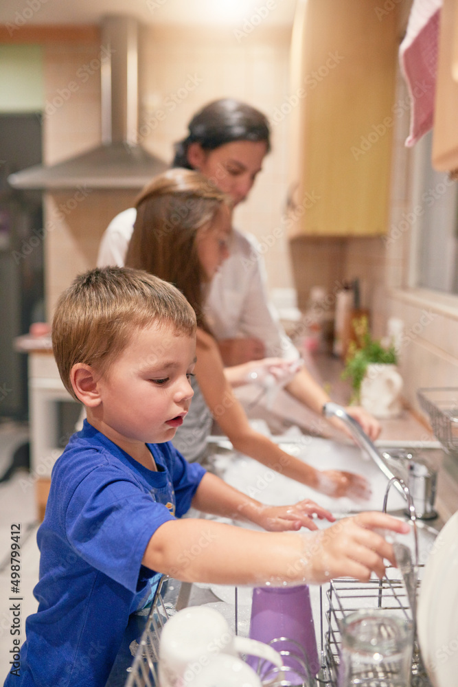 Many hands at work. Shot of a little boy washing dishes with his family at a kitchen sink.