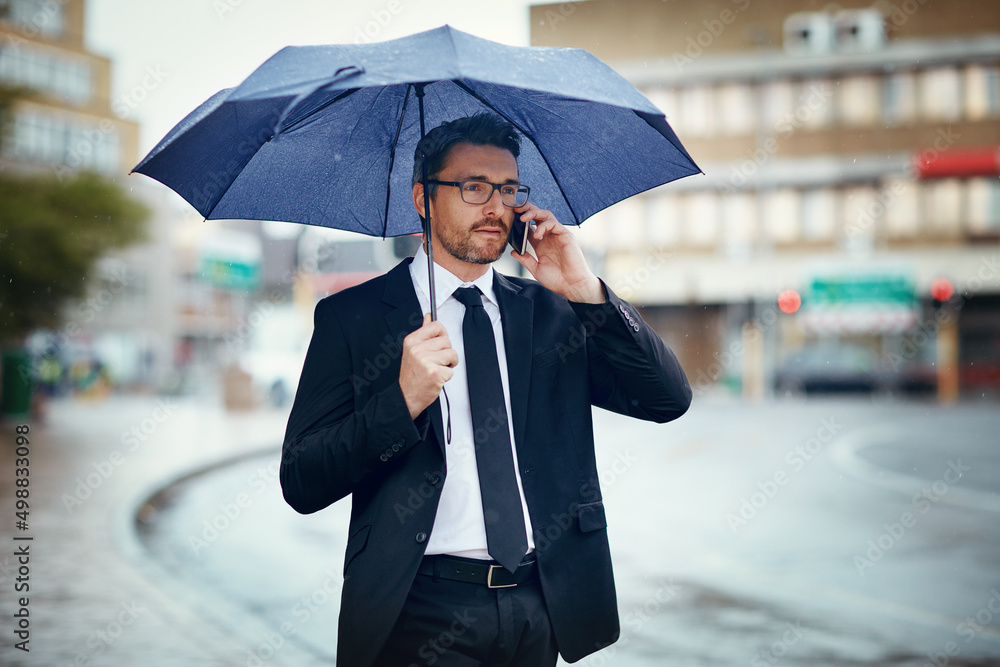 我很快就会到办公室。一个成熟的商人拿着雨伞打电话的镜头