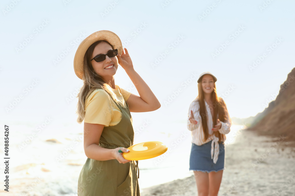 快乐的年轻女人和朋友在海边玩飞盘