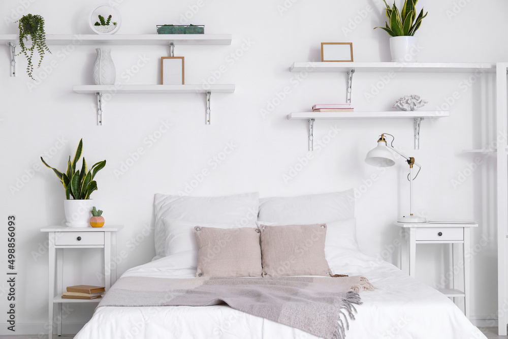 Comfortable bed, nightstands, houseplants and lamp near white wall