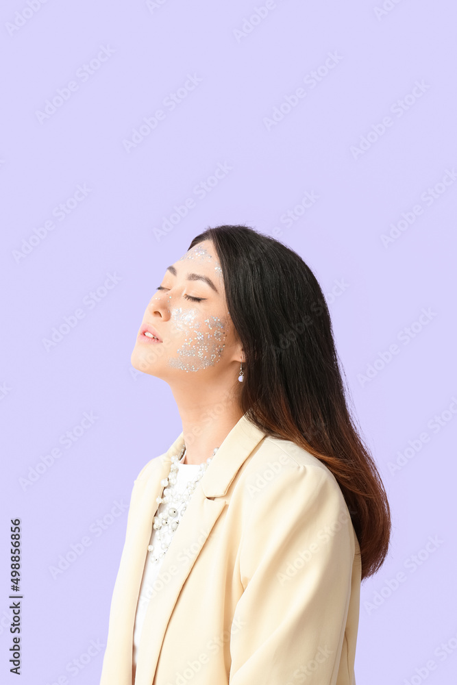 Elegant Asian woman with closed eyes and glitter makeup on color background