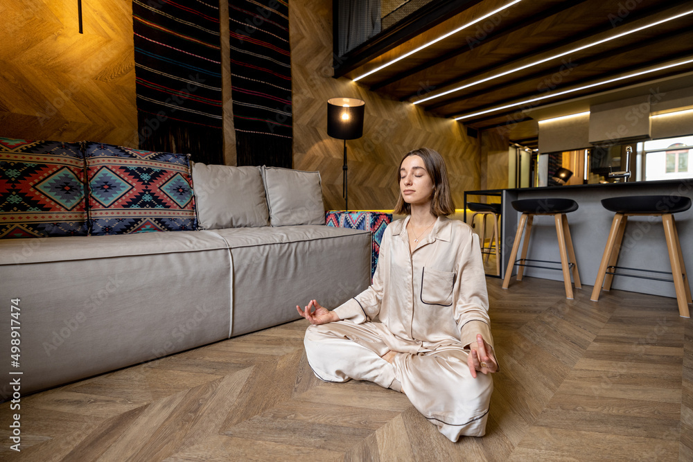 Relaxed woman feeling calm while meditating at modern apartment alone. Concept of mental health and 