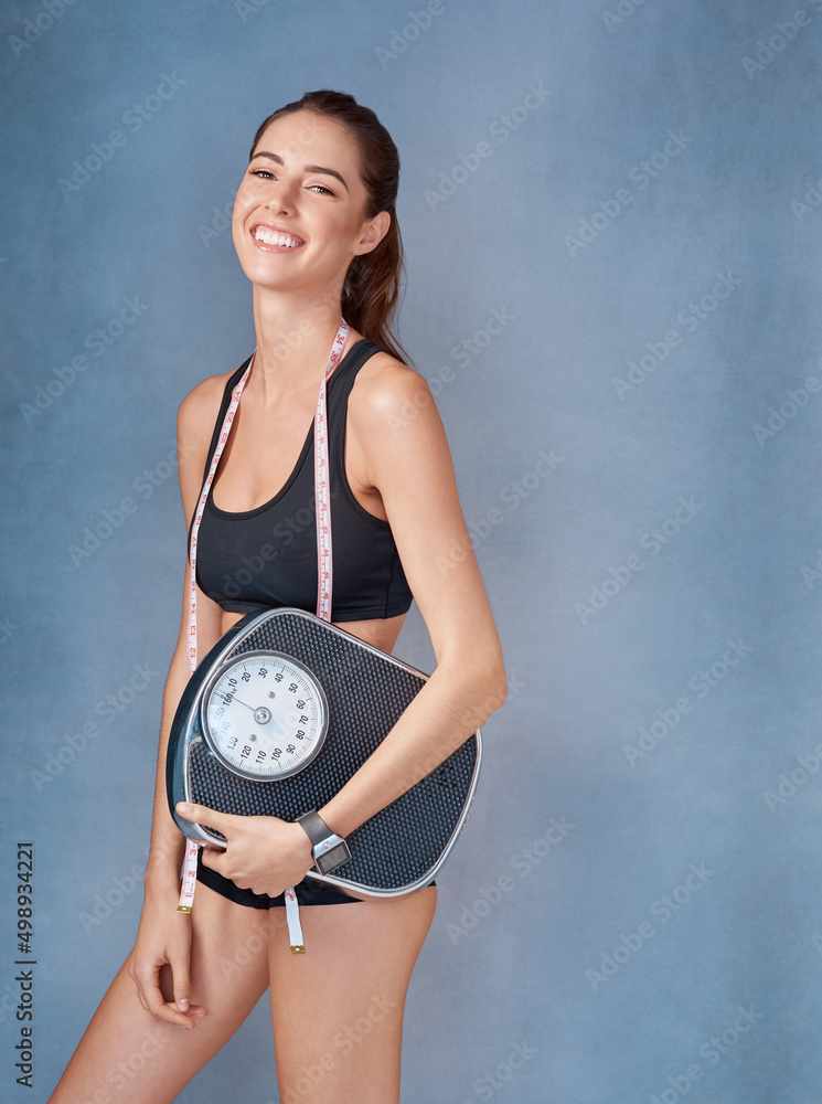 Getting closer to to my goals. Studio portrait of a sporty young woman holding a scale against a gre