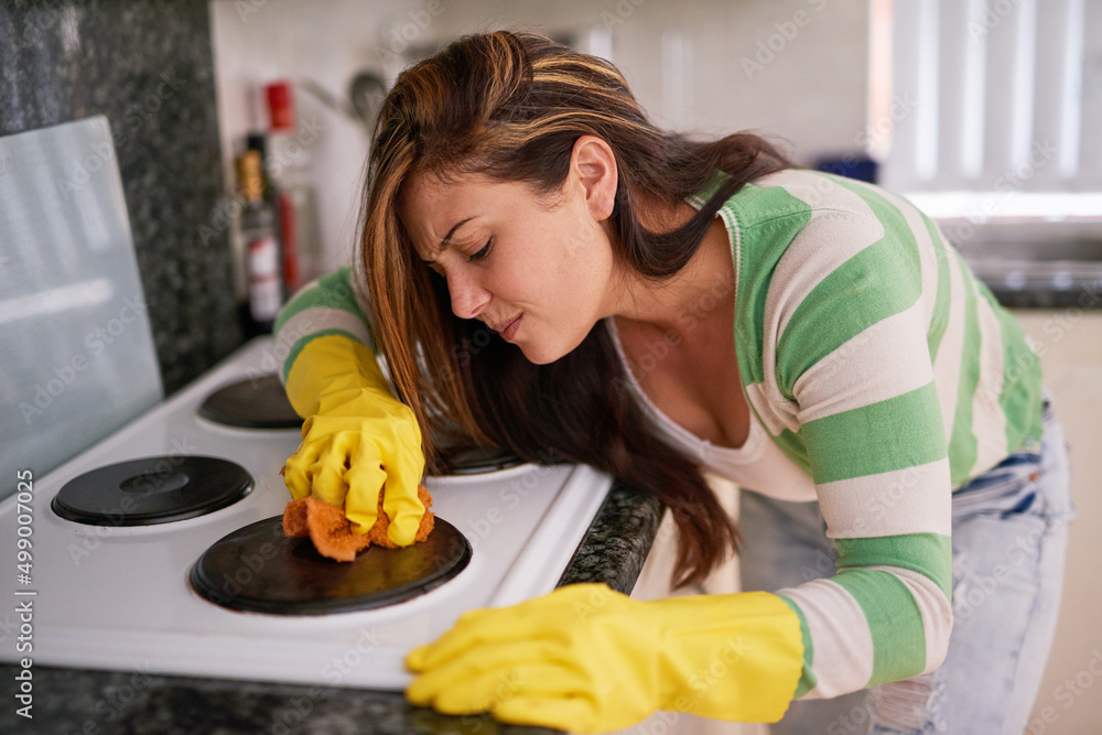 This grime just wont come off. Shot of a young woman cleaning a kitchen stove top.