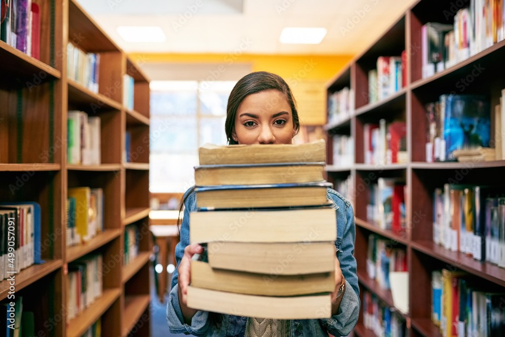 Its a stack of knowledge. Portrait of a university student holding a pile of books in the library at