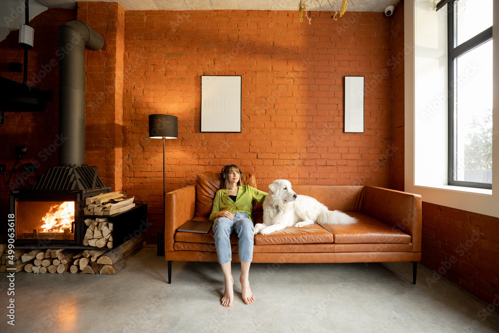 Young woman relax and listen to the music while sitting with her cute white dog on a couch at home. 