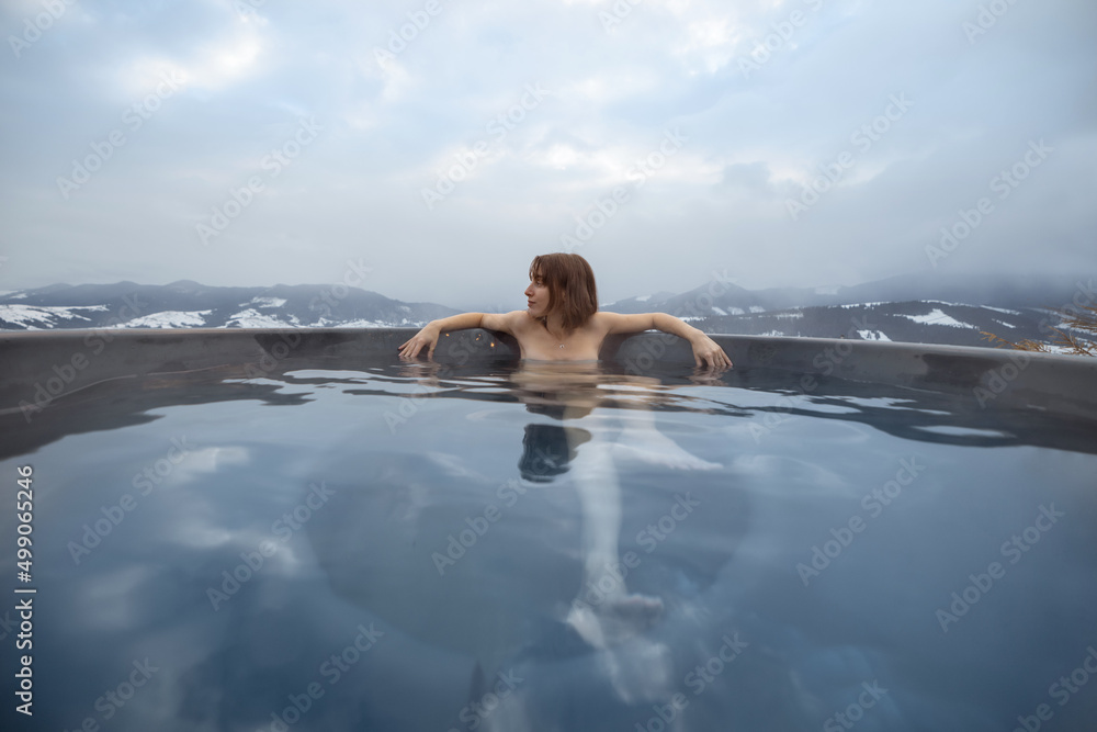 年轻女子冬天在山上的热水浴缸里洗澡。在热水浴缸里休息和恢复的概念