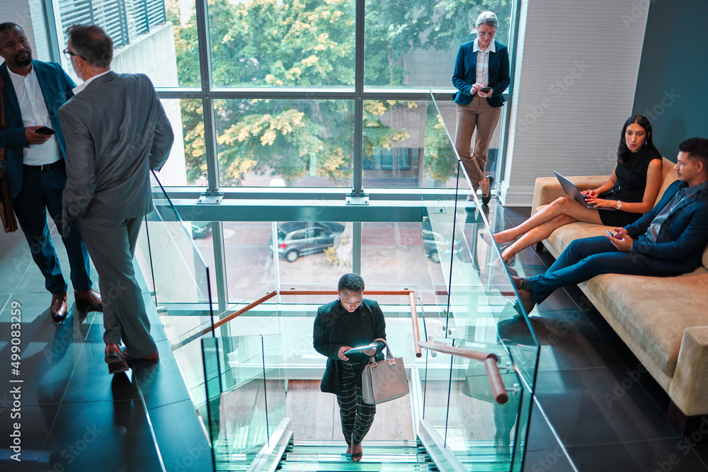 Lets get this day started. Shot of a young businesswoman walking up the stairs while using a digital