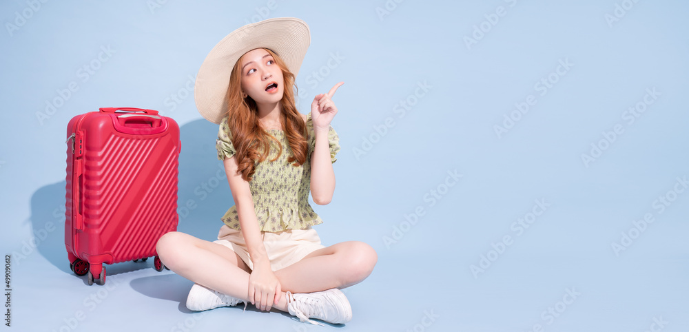 Full length image of young Asian girl with suitcase on blue background, travel concept