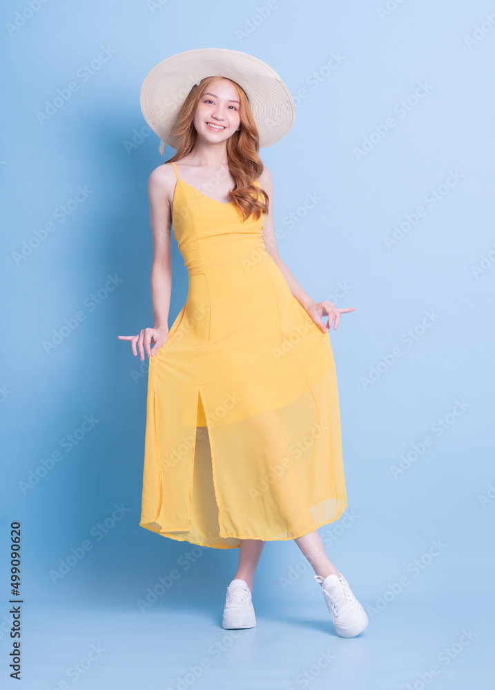 Full length image of young Asian woman wearing yellow dress on blue background