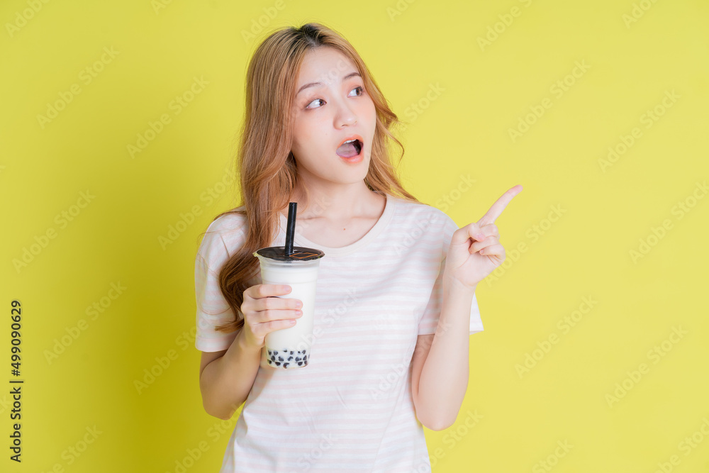 Image of young Asian girl drinking milk tea on yellow background