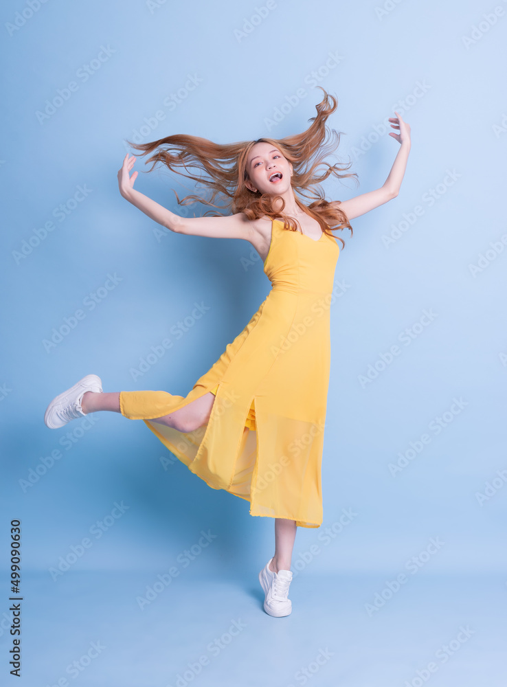 Full length image of young Asian woman wearing yellow dress on blue background