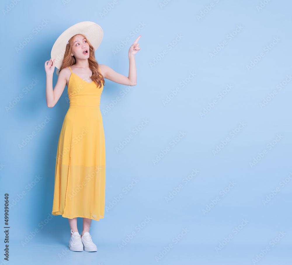 Full length image of young Asian woman wearing yellow dress on blue background