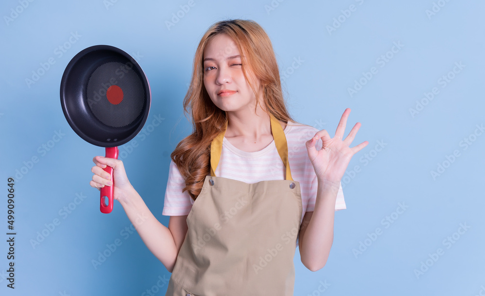 Image of young Asian woman holding pan on blue background