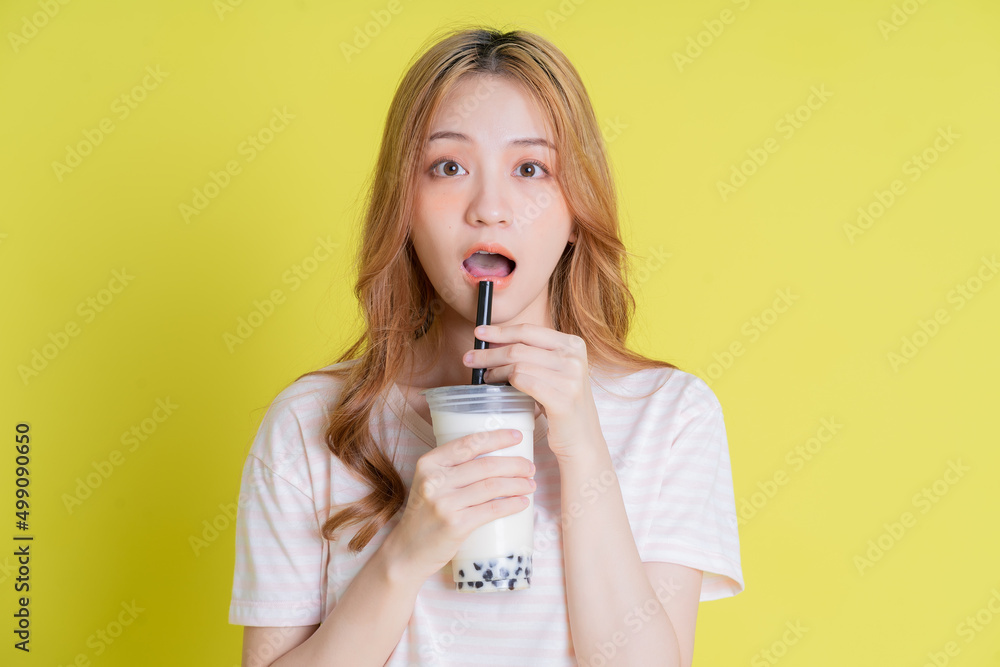 Image of young Asian girl drinking milk tea on yellow background