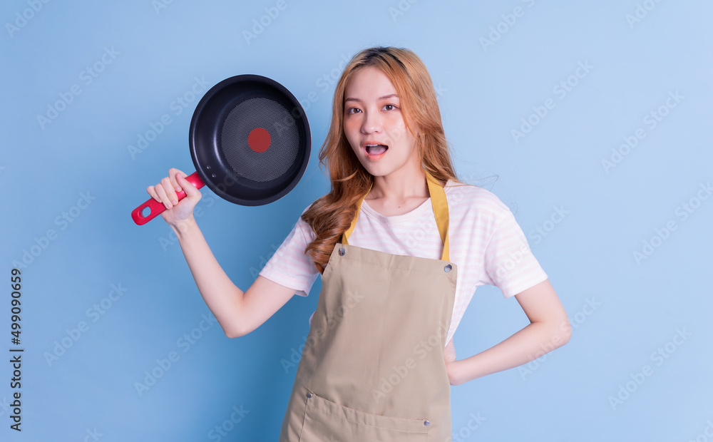 Image of young Asian woman holding pan on blue background