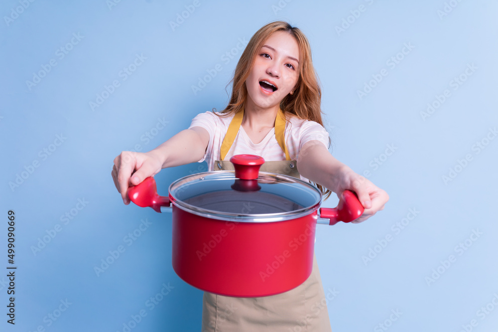 Image of young Asian woman holding pot on blue background