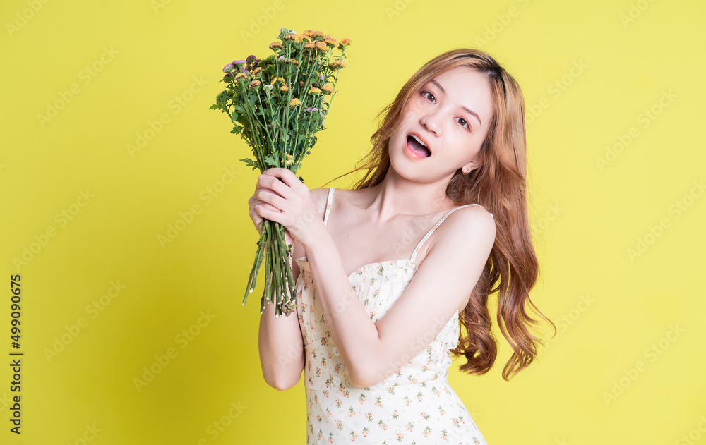 Image of young Asian woman holding flowers on yellow background