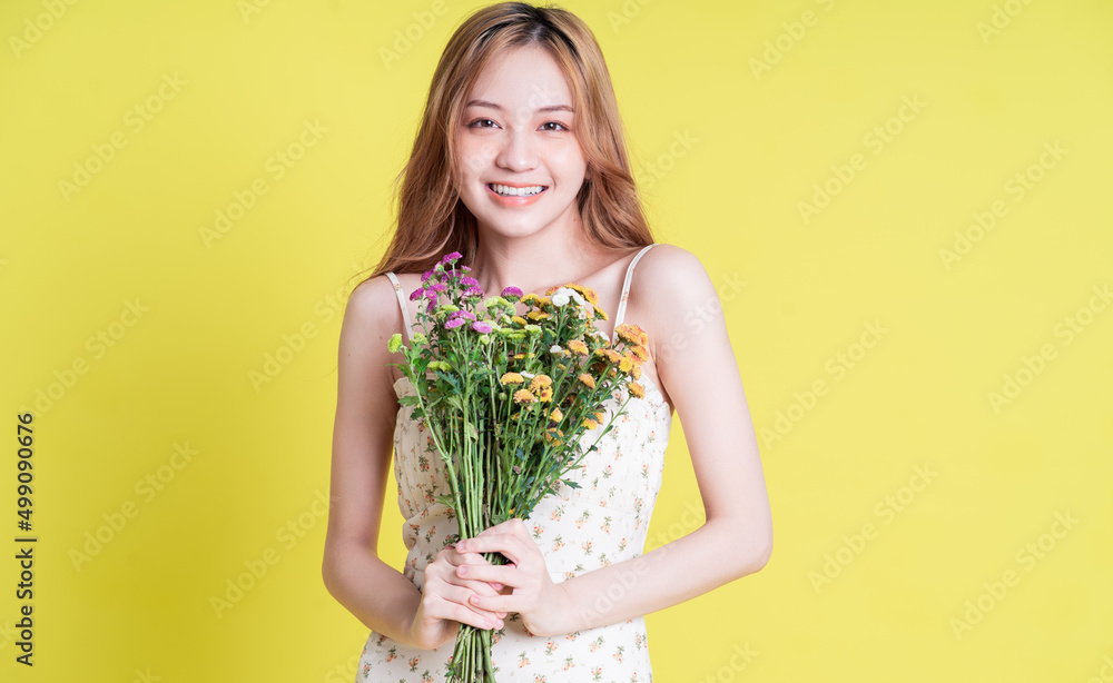 黄色背景下年轻的亚洲女子手捧鲜花的照片