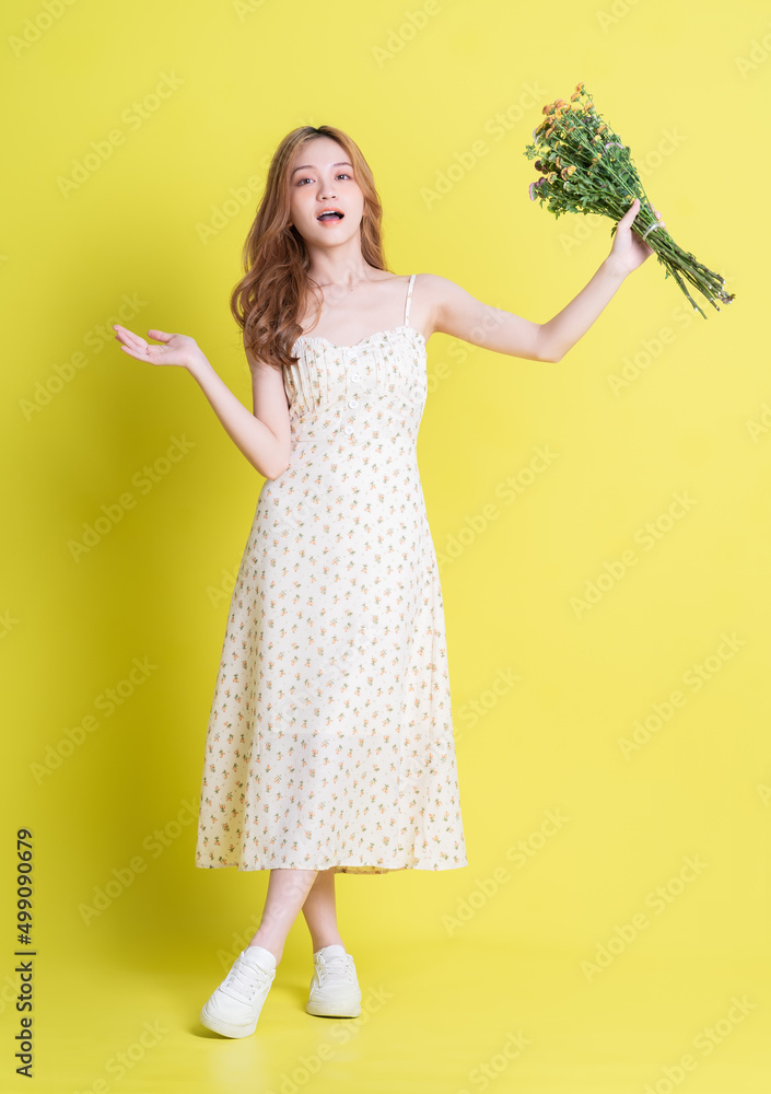 Image of young Asian woman holding flowers on yellow background