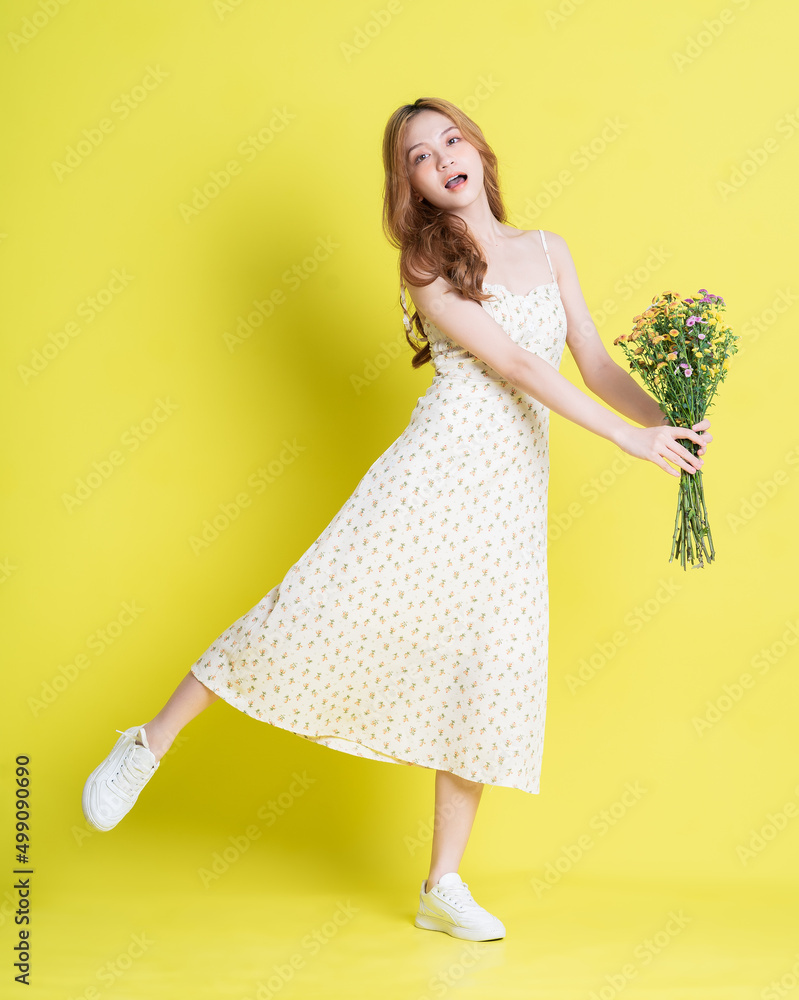 Image of young Asian woman holding flowers on yellow background