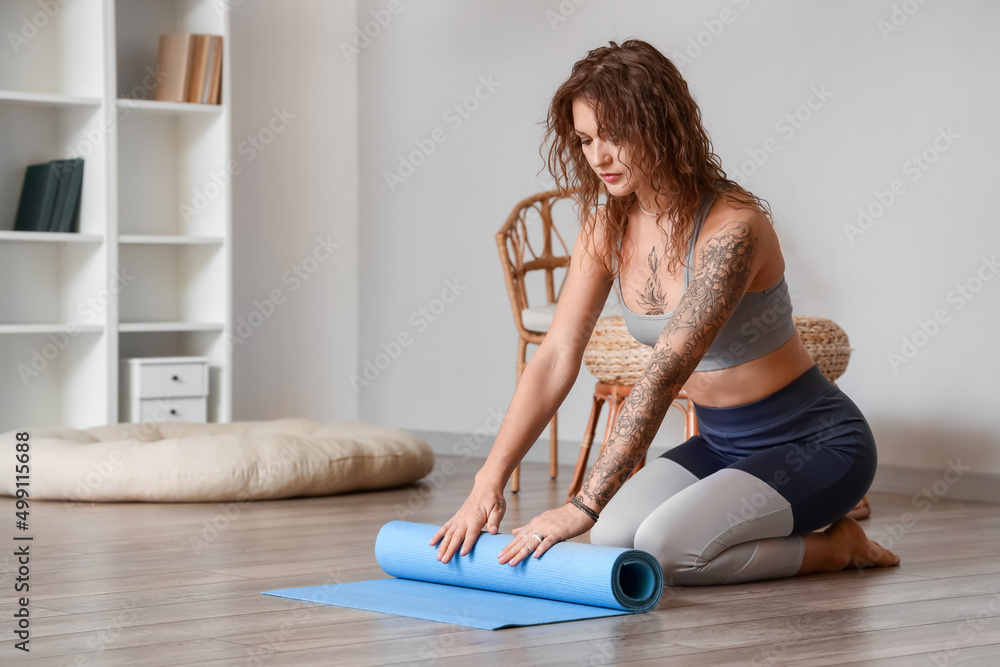 Beautiful tattooed woman with yoga mat at home