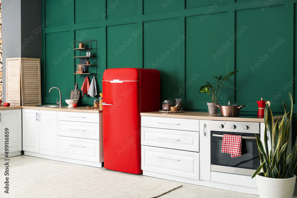 Stylish refrigerator and counters near green wall in kitchen