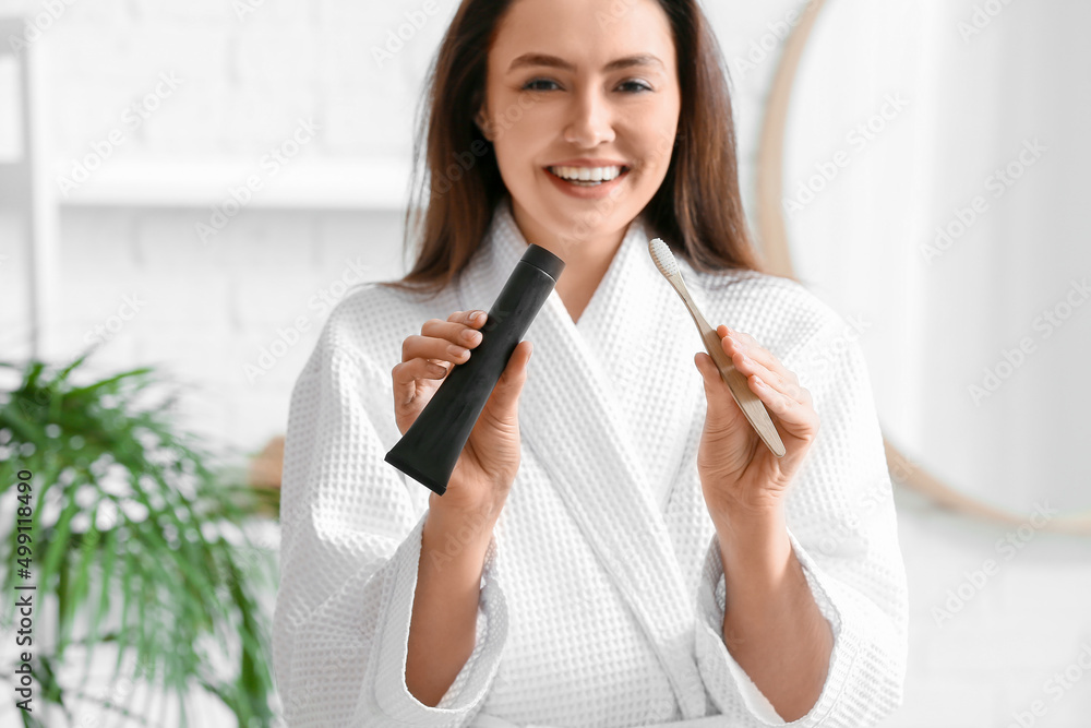 Beautiful young woman with activated charcoal tooth paste and brush in bathroom